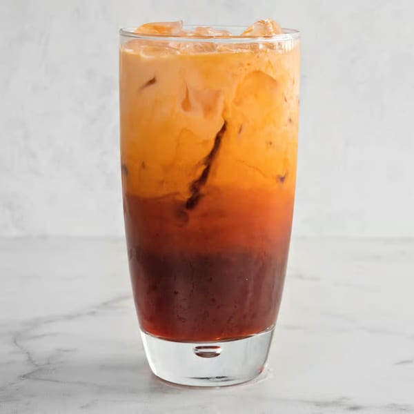 A tall glass of iced Vietnamese Thai tea with distinct layers of dark tea and creamy orange.
