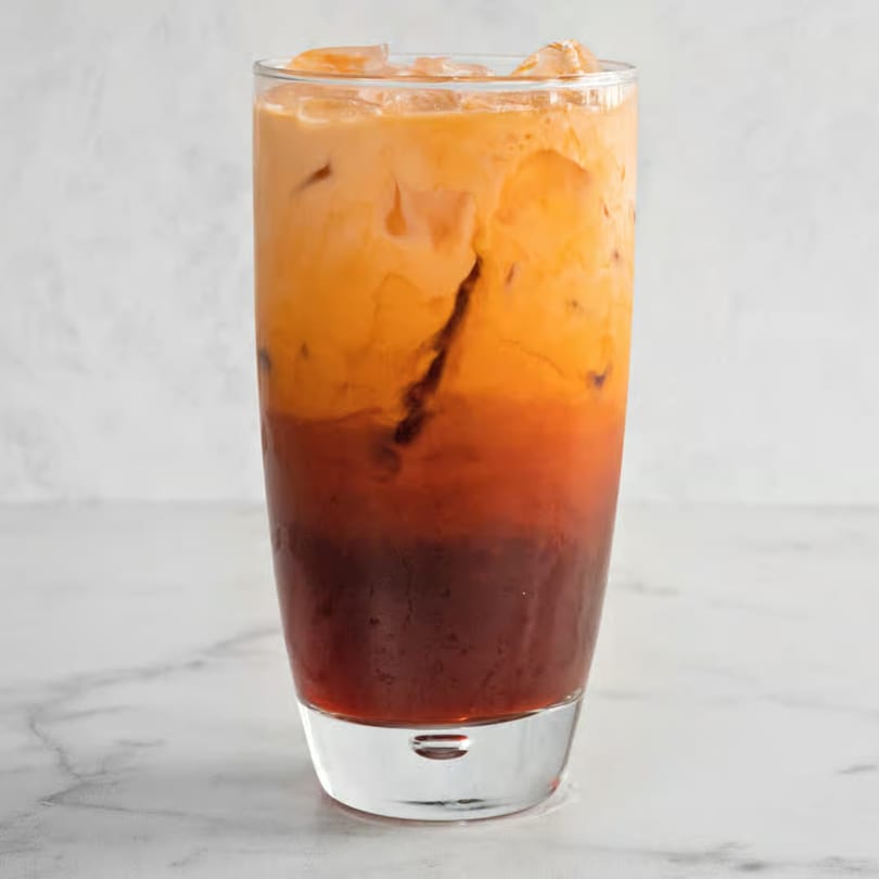 A tall glass of iced Vietnamese Thai tea with distinct layers of dark tea and creamy orange.
