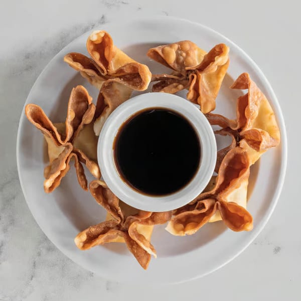 Crispy fried wontons arranged around a small white bowl of dark dipping sauce on a white plate.