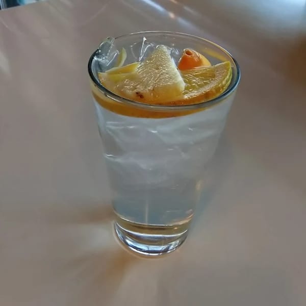A clear glass of iced water with lemon and orange slices on a light-colored table.