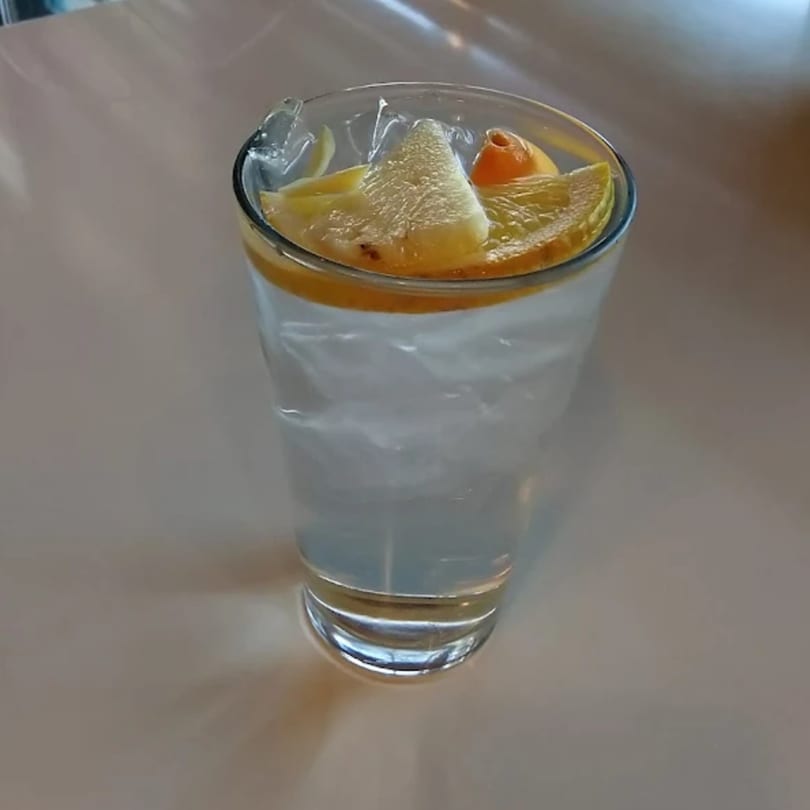 A clear glass of iced water with lemon and orange slices on a light-colored table.