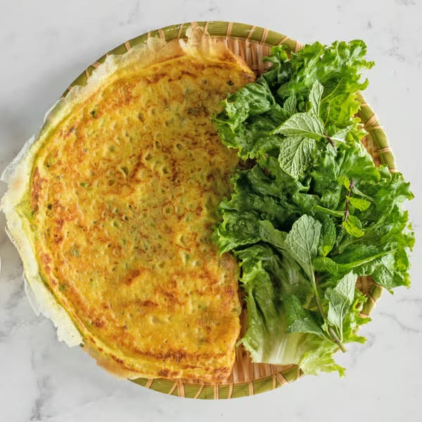 A Vietnamese savory crepe (Banh Xeo) and a side of fresh lettuce and mint on a woven tray.