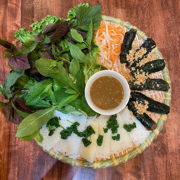 A Vietnamese dish with various herbs, rice vermicelli, pickled vegetables, and grilled beef in betel leaves.