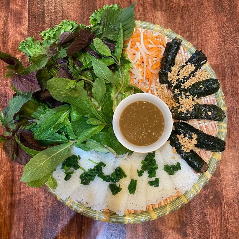 A Vietnamese dish with various herbs, rice vermicelli, pickled vegetables, and grilled beef in betel leaves.