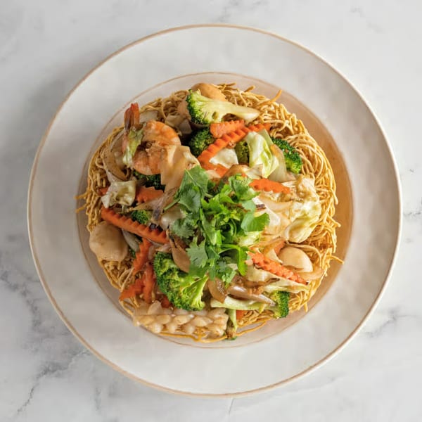 Crispy Vietnamese egg noodles topped with shrimp, broccoli, carrots, and cabbage on a white plate.