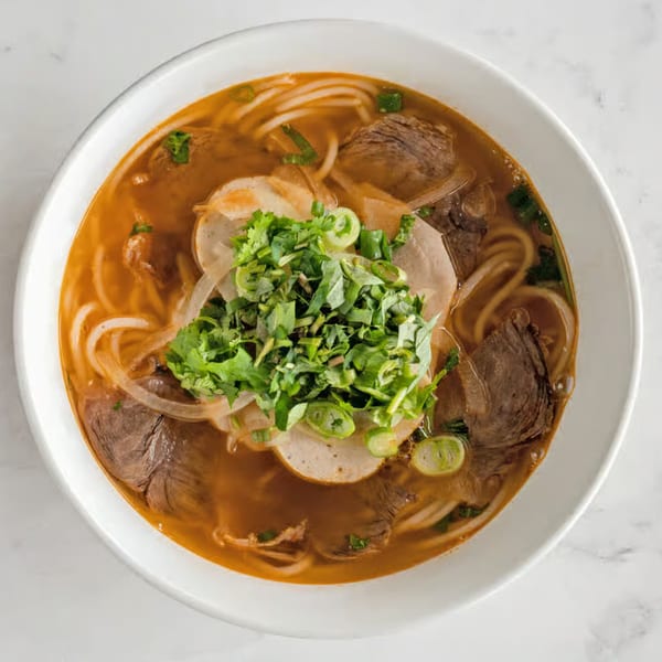 Overhead view of a bowl of Vietnamese Bun Bo Hue with beef, pork, noodles, and herbs.