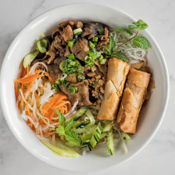 Vietnamese vermicelli bowl with grilled pork, spring rolls, pickled vegetables, and fresh mint.