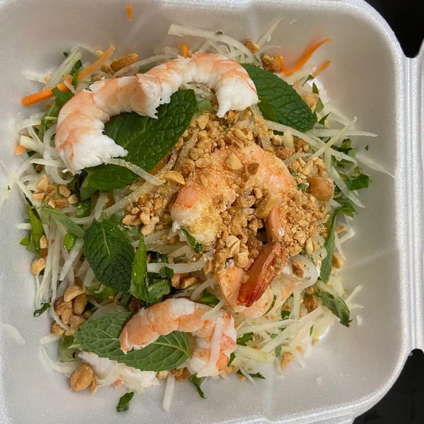 Vietnamese shrimp salad with shredded papaya, carrots, mint, and crushed peanuts in a white takeout container.